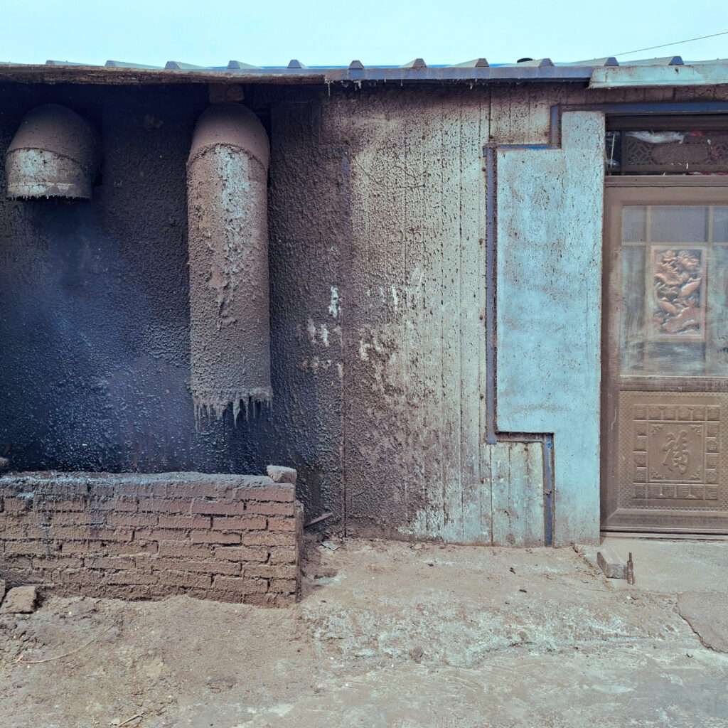 Exterior of a burnt, soot-covered building with two curved vents and a blue weathered door beside it