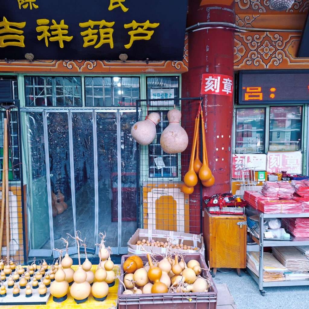 Shopfront with hanging gourds and crate of small gourds for sale, Chinese signage above.