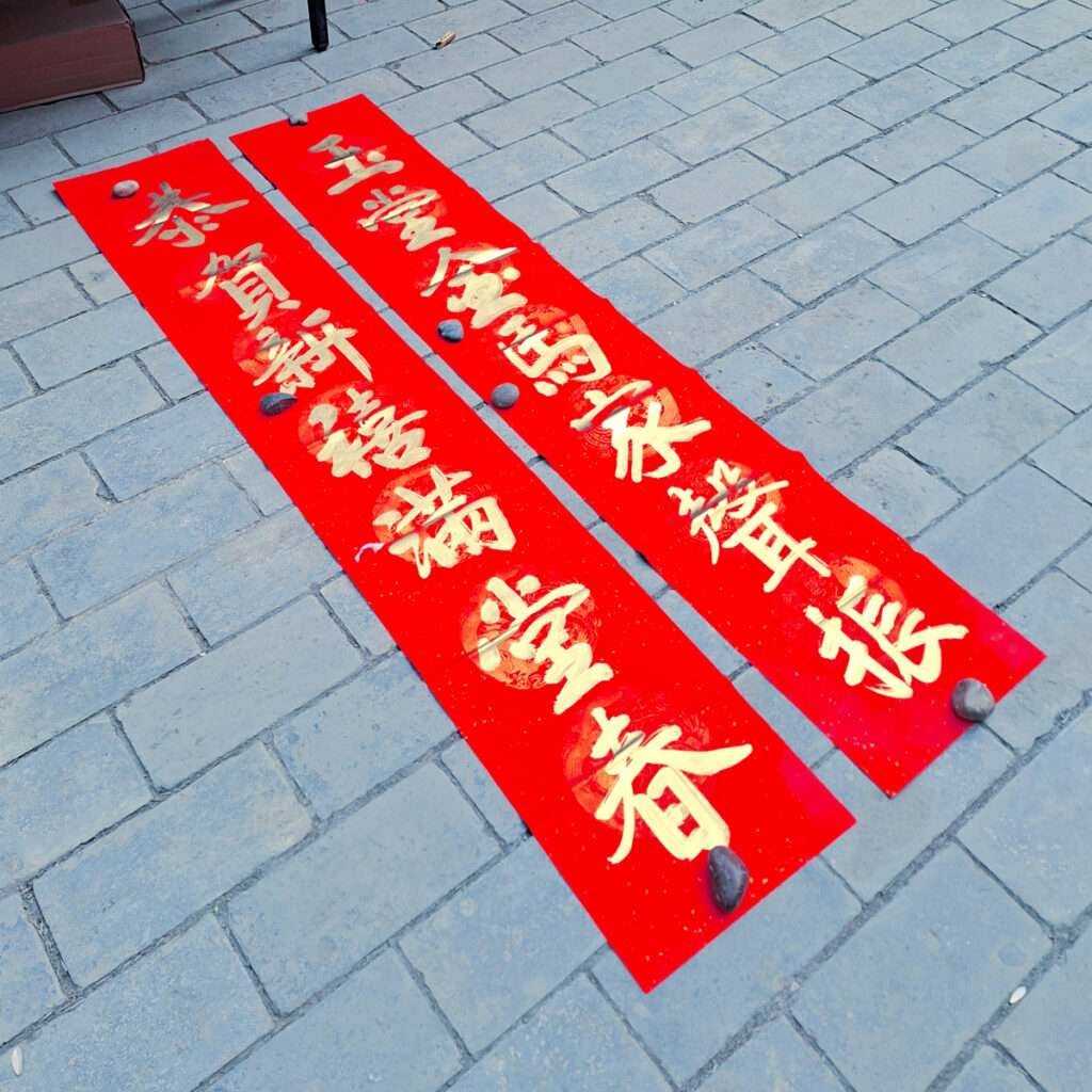 Two red vertical banners with gold Chinese writing laid on a gray brick sidewalk.