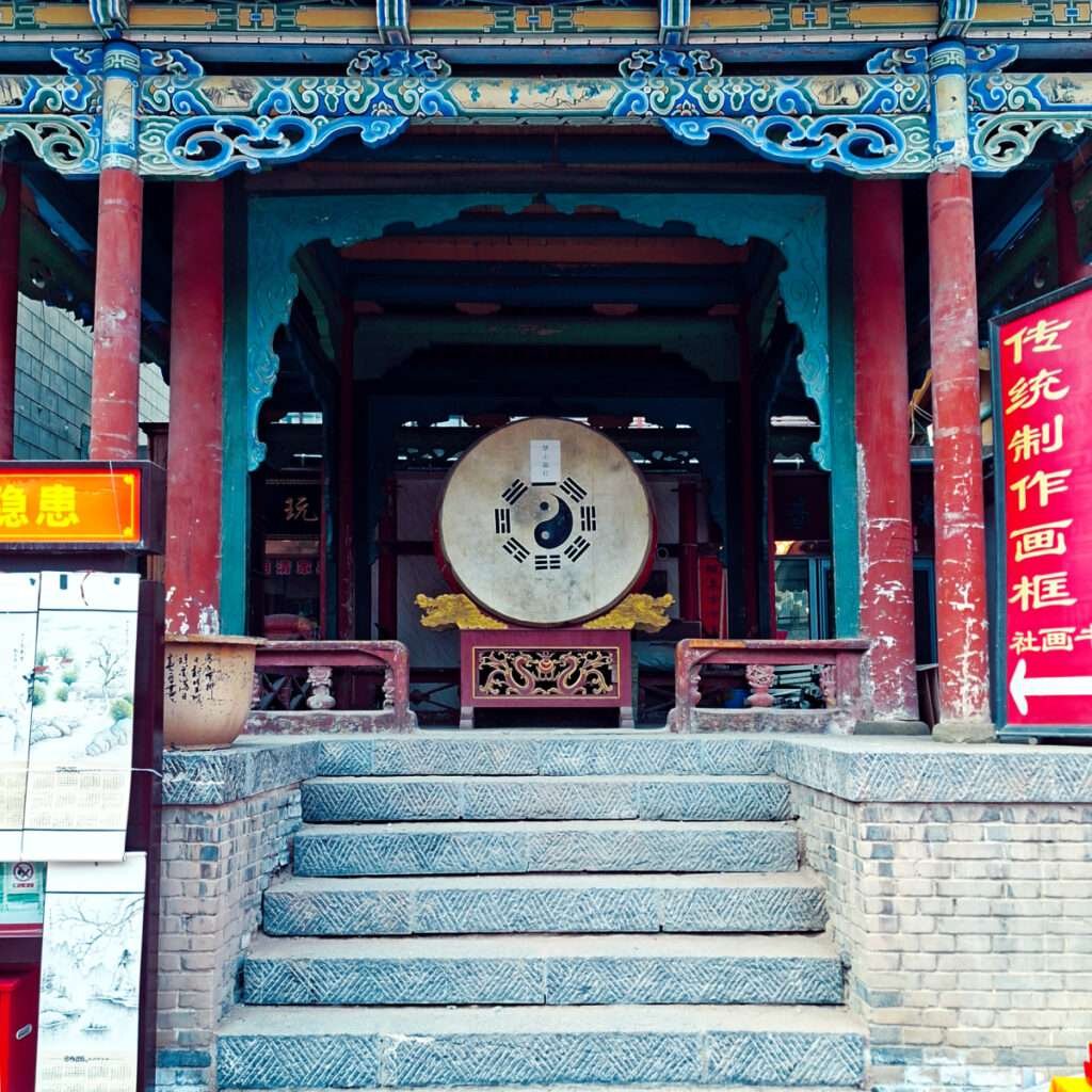 Front view of a traditional Chinese temple entrance with a large drum on a carved pedestal, red pillars, and blue ornate beams.