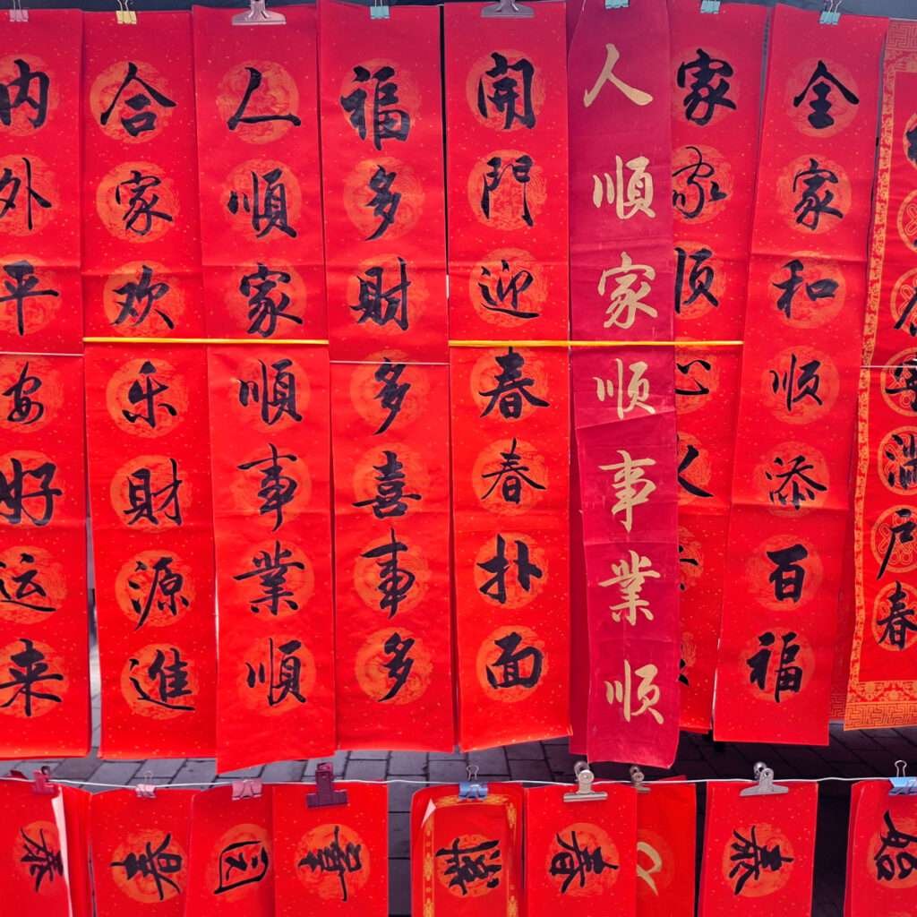 Rows of red vertical banners with black Chinese calligraphy for Lunar New Year, hung in a market display