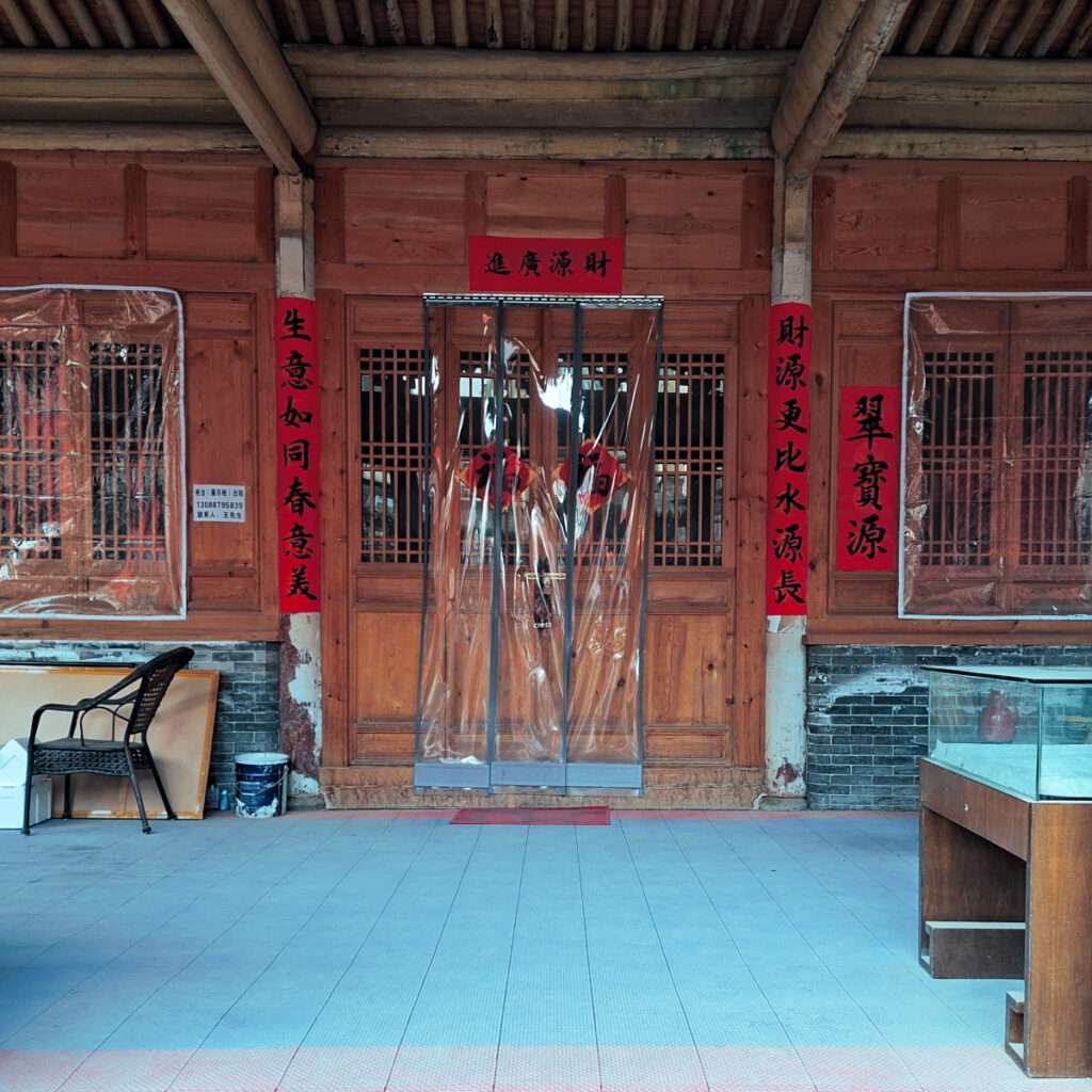 Wooden doorway with red couplets on either side, a clear plastic curtain in the entrance, and signs above and beside the door.