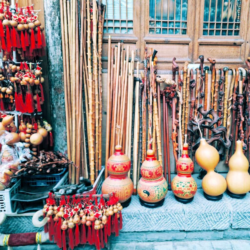 Street market stall displaying tall wooden canes and carved staffs with red tassels and traditional gourds on the ground.