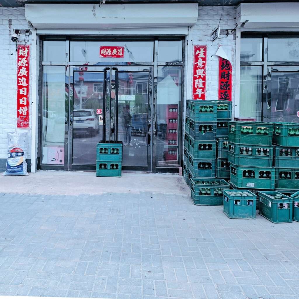 Storefront with glass doors and red Chinese banners, stacked green crates outside