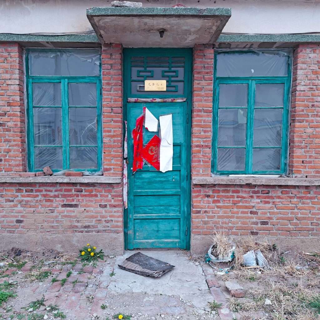 Old brick building with a teal door, torn posters, and cracked sidewalk debris outside.