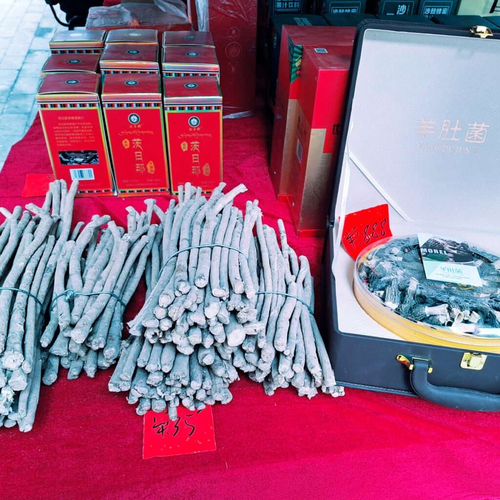 Bundles of gray incense sticks tied with string, displayed on a red cloth with red boxes and an open case nearby in a market stall