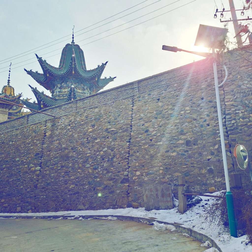 Stone city wall with ornate Chinese temple roofs peeking above, sun glare in the corner