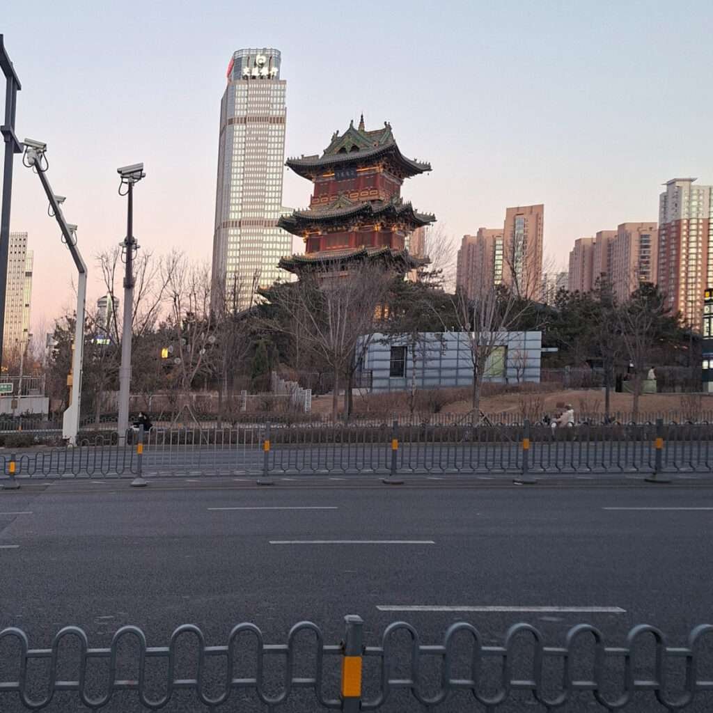 Traditional multi-tier Chinese pagoda in a city park with modern skyscrapers behind.