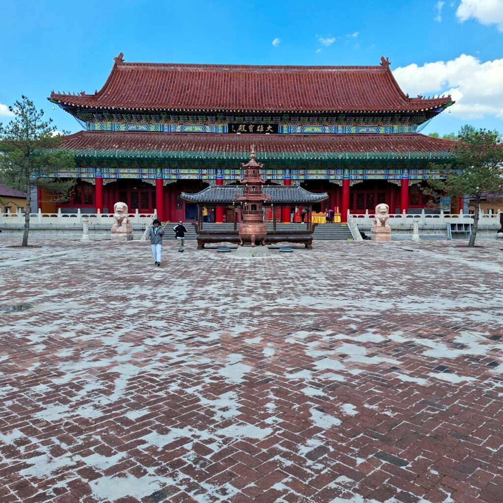 Traditional Chinese temple with ornate green-and-gold eaves, red columns, and a large bronze incense burner in the courtyard.