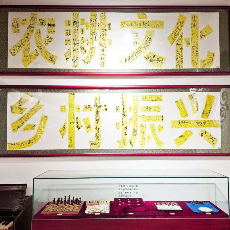 Two white panels filled with handwritten Chinese characters on yellow tape, framed on the wall above a glass display case.