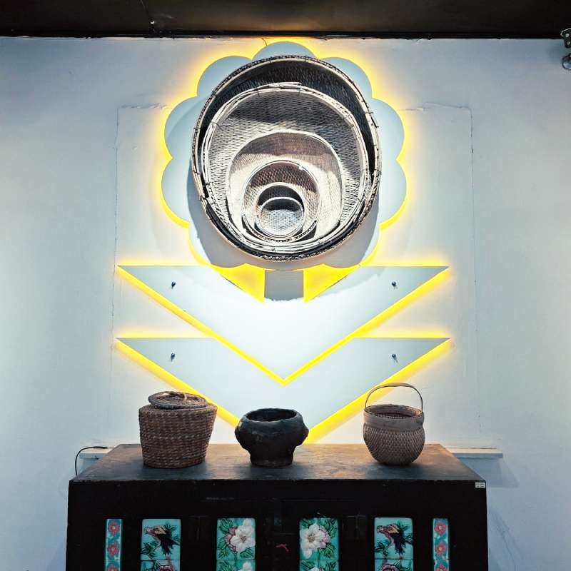 Art installation: a large woven basket sculpture mounted on a neon yellow chevron wall, with three baskets on a table below.