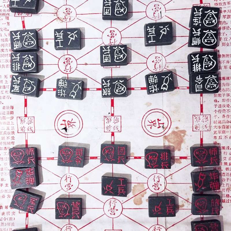 Chinese strategy game board with black tiles bearing white inscriptions placed on a red-lined grid; various symbols visible on tiles and intersections.