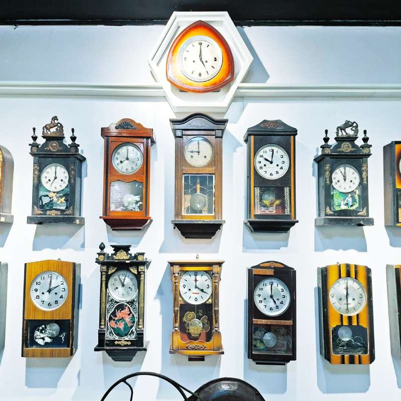 Row of vintage wall clocks mounted on a light blue wall, including ornate and wooden cases as a centerpiece clock sits at top.
