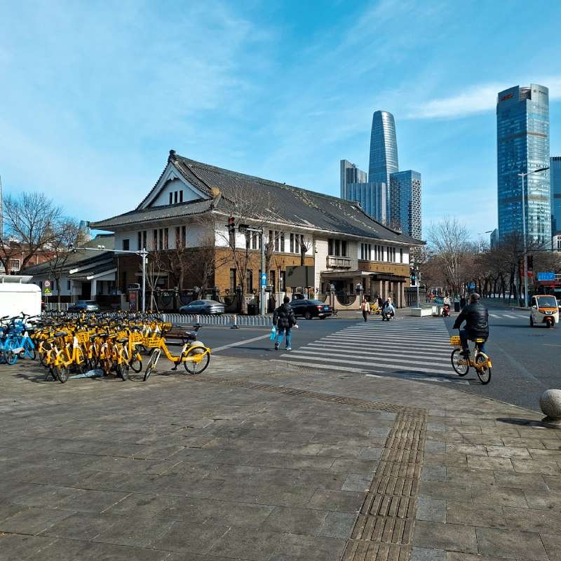 Crosswalk scene with a traditional building, yellow bike-share bikes on the left, and tall modern skyscrapers in the background.