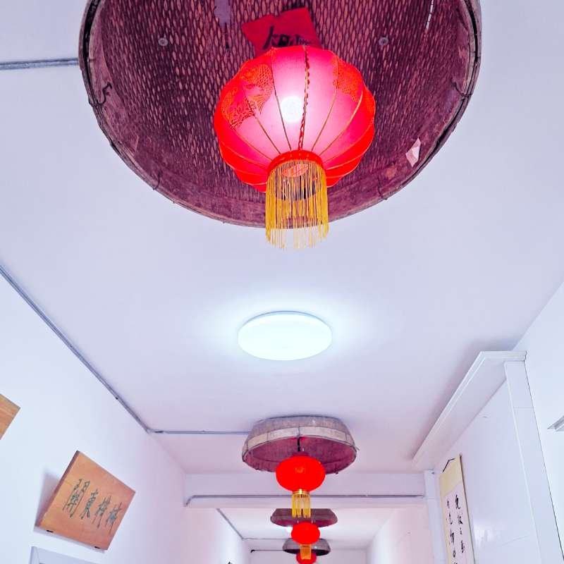 Red Chinese lanterns hang from the white ceiling along a bright hallway. A round ceiling light is visible above them.