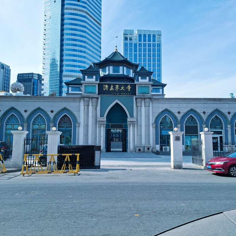 Gate to a Chinese-style building with blue-tiled arches, set against modern high-rises; Chinese signage above the entrance shows the name of the place.