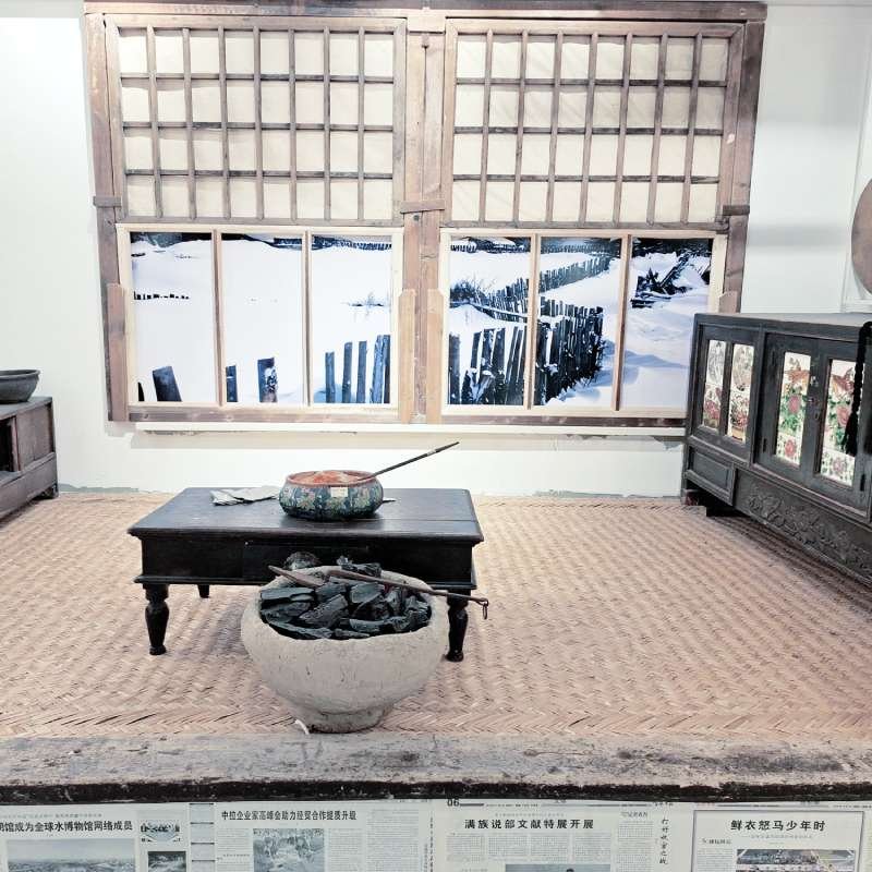 Museum-style interior showing wooden lattice windows, a low dark table, and a coal brazier; snow-covered landscape visible through the windows.