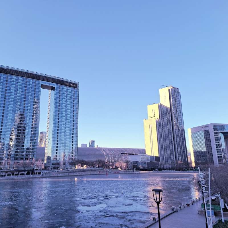 City skyline by a frozen waterway with tall glass office buildings under a clear blue sky.