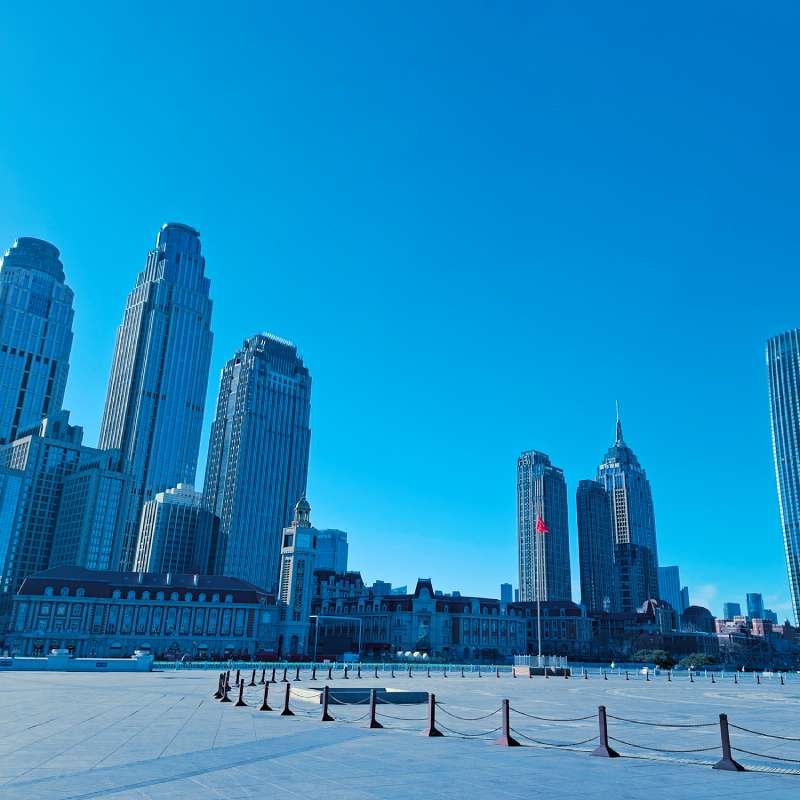 City skyline with tall glass skyscrapers against a clear blue sky; a fenced promenade with rope posts in the foreground.
