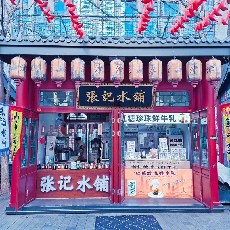 Traditional Chinese beverage shop in a red storefront with hanging lanterns and gold Chinese signage; open counter with jars and drinks on display