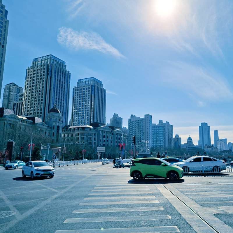 City street with tall modern buildings under a bright blue sky; a bright green car crosses a zebra-crossing in the foreground.