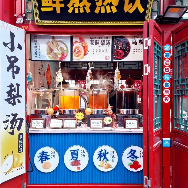 Street juice stall with three tall beverage dispensers and red storefront, multiple Chinese signs above and around.