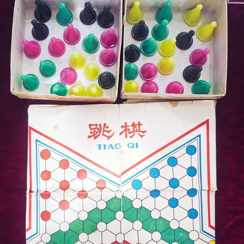 Two open boxes hold many colorful Chinese checkers marbles (pink, yellow, green, black) above a folded game board labeled 'TIAO QI' in red Chinese characters.
